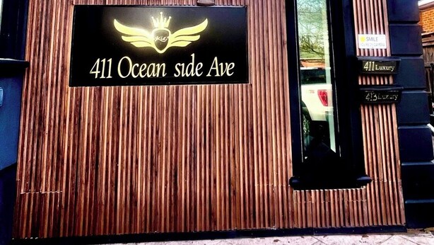 Eine Gebäudefassade mit vertikaler Holzpaneelausstattung, einem Schild mit der Aufschrift '411 Ocean side Ave' und einem kleinen Fenster.