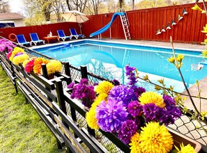 A swimming pool with a slide, surrounded by a wooden fence and colorful flowers. - Enjoyable 1-bedroom house with AC in Richmond Hill (Richmond Hill)
