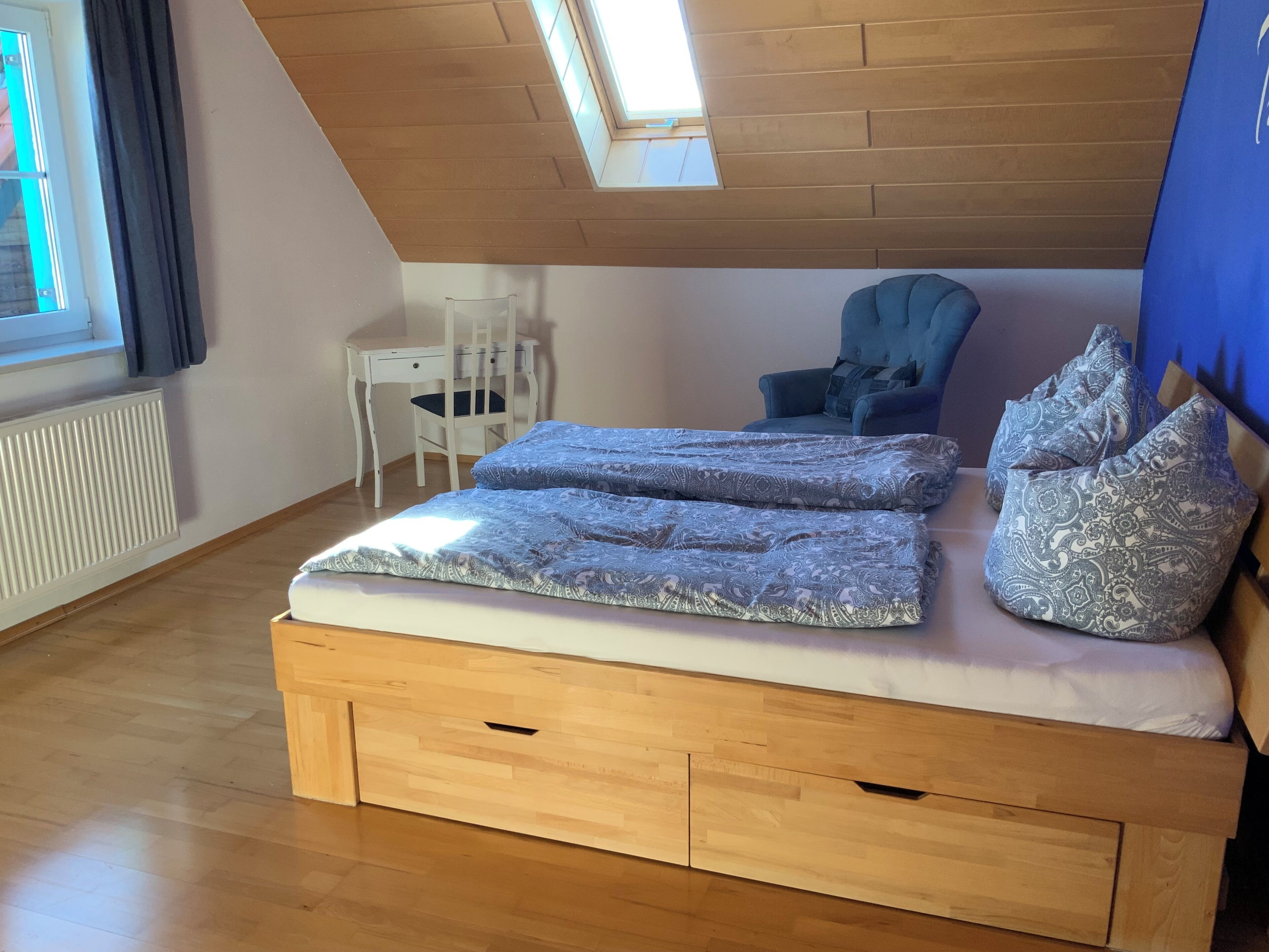 Une chambre de style « loft », avec un plafond en pente, un cadre de lit en bois, un bureau et une chaise.