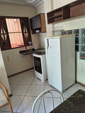 A compact kitchen with a gas stove, a white refrigerator, and a window with bars. - Comfortable ground-floor apartment facing the street, 10 minutes from the beautiful Itaparica beach. (Vila Velha)