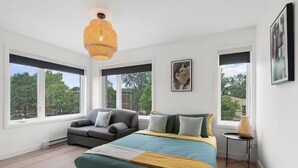 A modern bedroom with a large bed, a sofa, and a view of trees through large windows.