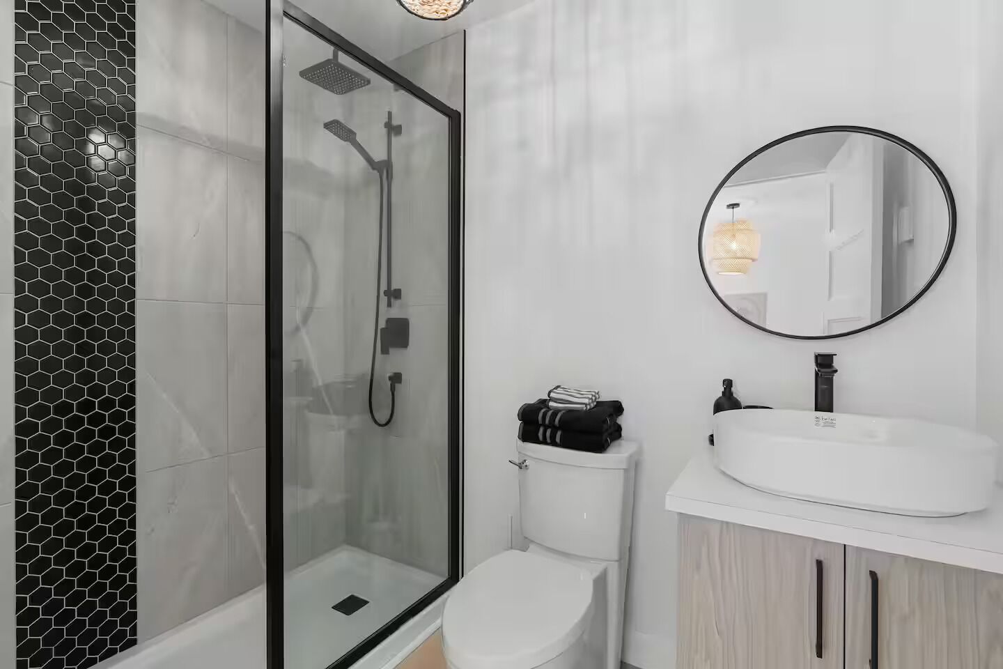 Ein modernes Badezimmer mit einer Duschkabine, einer weißen Toilette und einem weißen Waschbecken mit rundem Spiegel.