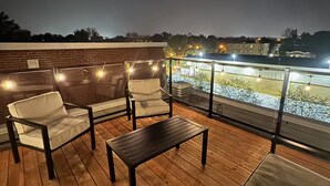 A rooftop deck with wooden flooring, cushioned chairs, and a small table.