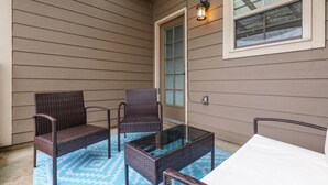 Une terrasse couverte, aménagée avec des meubles en osier et une table en verre.