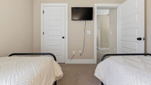 Un dormitorio con dos camas, un televisor montado en la pared y una puerta que da a otra habitación.