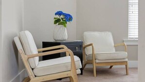 Une pièce comprenant deux fauteuils blancs à revêtement en tissu, un petit vase blanc orné de fleurs bleues et une table d  ’appoint en bois foncé.