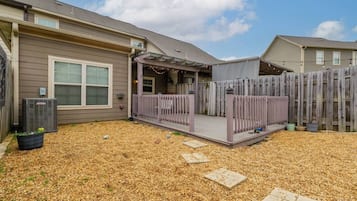 A residential backyard with a covered patio area, a wooden fence, and a gravel ground.