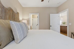 A bedroom with a bed, pillows, a nightstand, a lamp, and a door leading to another room.