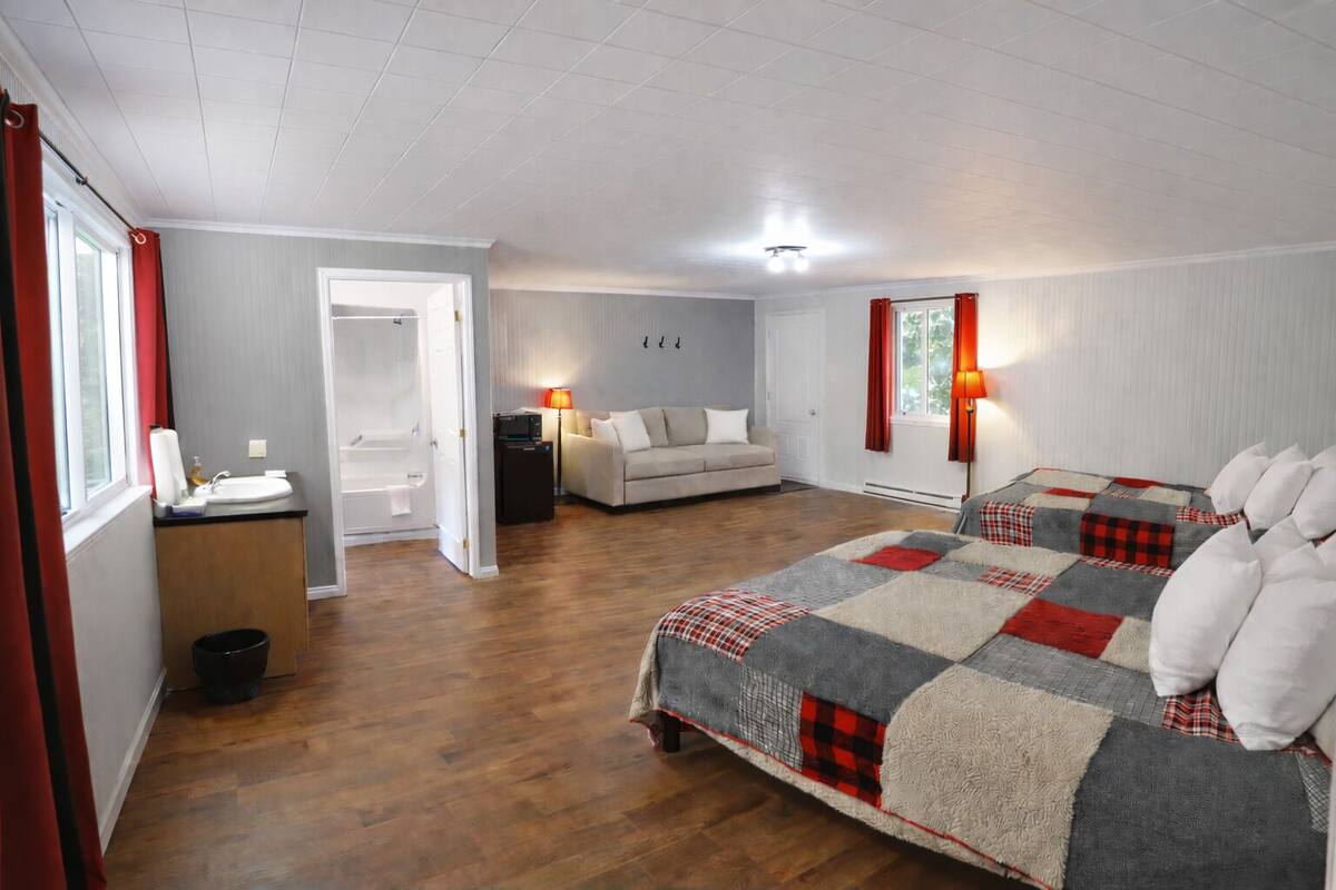 A bedroom with a large bed, a sofa, a small table, a lamp, and a bathroom with a shower and toilet.