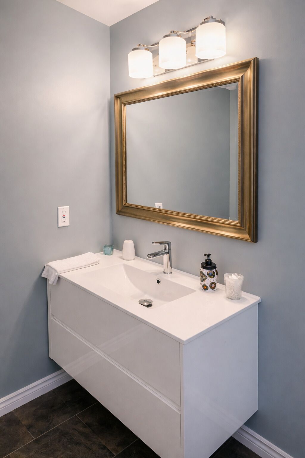 A bathroom with a white vanity, a gold-framed mirror, and a light blue wall.