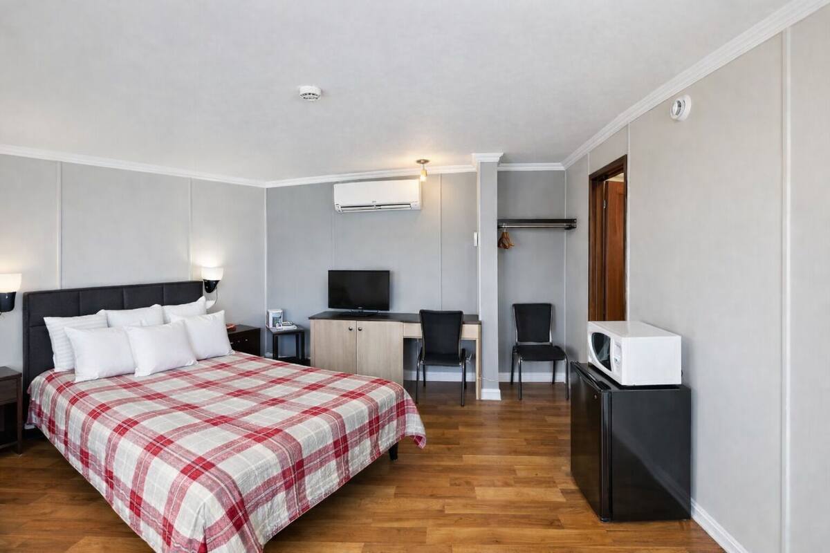 A hotel room with a bed, a desk with a computer, a chair, a TV, and a microwave.