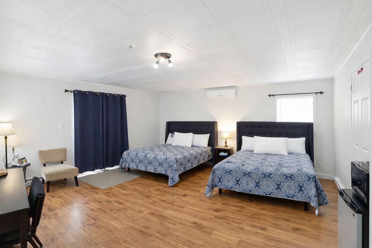 A room with two beds, a desk, a chair, a TV, and a fireplace.