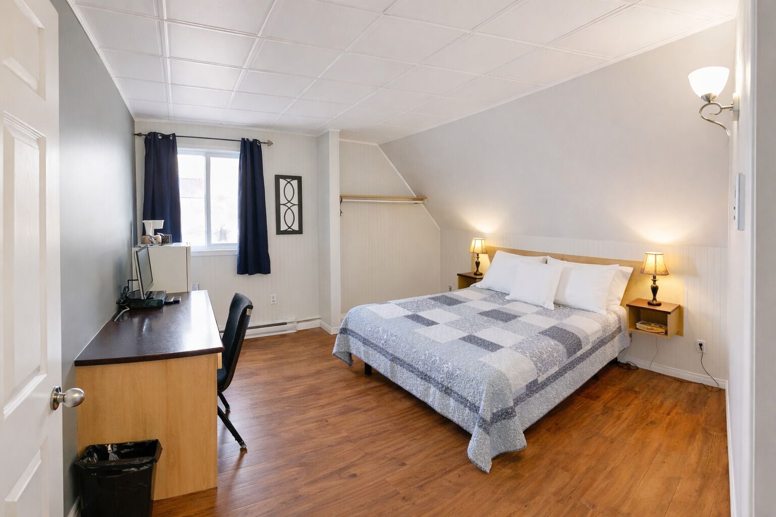 Een slaapkamer met een bed, nachtlampjes, een bureau en een stoel.