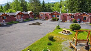 A row of red cabins with orange trim, a picnic table, and a swing set in a grassy area with a paved parking lot. - Motel Au Vieux Frontenac (Thetford Mines)