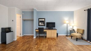 A compact room with a wooden floor, a desk with a computer, a chair, a small fridge, a lamp, and a chair. - Motel Au Vieux Frontenac (Thetford Mines)