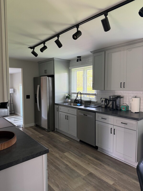 A modern kitchen with white cabinetry, a stainless steel refrigerator, and a black countertop. - Cozy 3-bedroom house in lovely Rochester with AC and charm (Rochester)