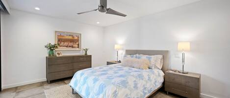 Un dormitorio con una cama, mesitas de noche, un ventilador de techo, un cuadro y un aparador.
