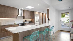 Eine moderne Küche mit Holzausstattung, einem Edelstahlkühlschrank, einer weißen Arbeitsplatte und türkisfarbenen Barhocker.