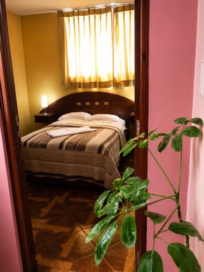 A hotel room with a bed, a nightstand, a lamp, a window with curtains, and a potted plant. - Hotel Tamaris Chiclayo (Chiclayo)