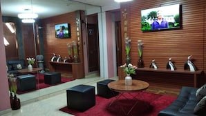 A modern hotel lobby with a red carpet, black sofas, a round coffee table, and a TV mounted on the wall.