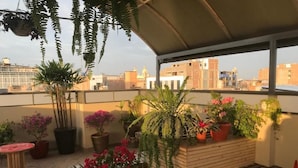 A rooftop terrace with potted plants, a wooden bench, and a table.