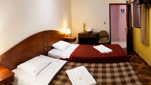 Ein Hotelzimmer mit einem hölzernen Kopfteil, einem Bett mit kariertem Bettbezug, einem Nachttisch mit Lampe, einem kleinen Tisch mit einer Vase und einem Sessel.