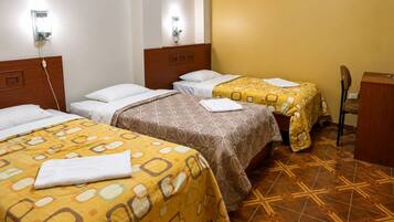 Una camera d'hotel con due letti, ciascuno con copripiumino decorato, una testiera in legno e un comodino con una lampada.