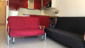 Un salon avec un canapé rouge et un canapé noir, une cuisine avec des placards rouges et un four à micro-ondes.