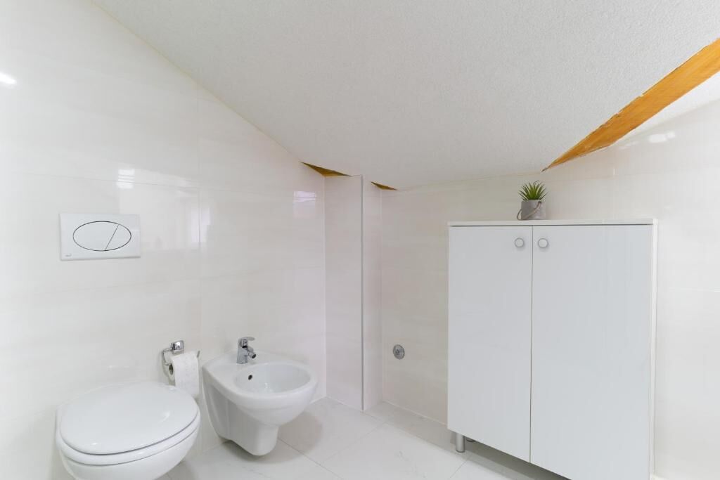 A modern bathroom with a toilet, bidet, and white cabinet.