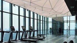 Una palestra moderna con tapis roulant e manubri, ampie finestre e un design geometrico del soffitto.
