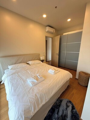 Une chambre d’hôtel avec un grand lit, une armoire, un appareil de climatisation et une petite poubelle.