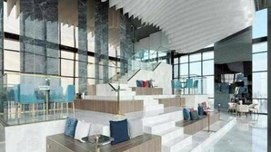 Un'ampia hall dall'arredamento moderno, con un'area salotto centrale dotata di divani e una scala che conduce ai piani superiori.