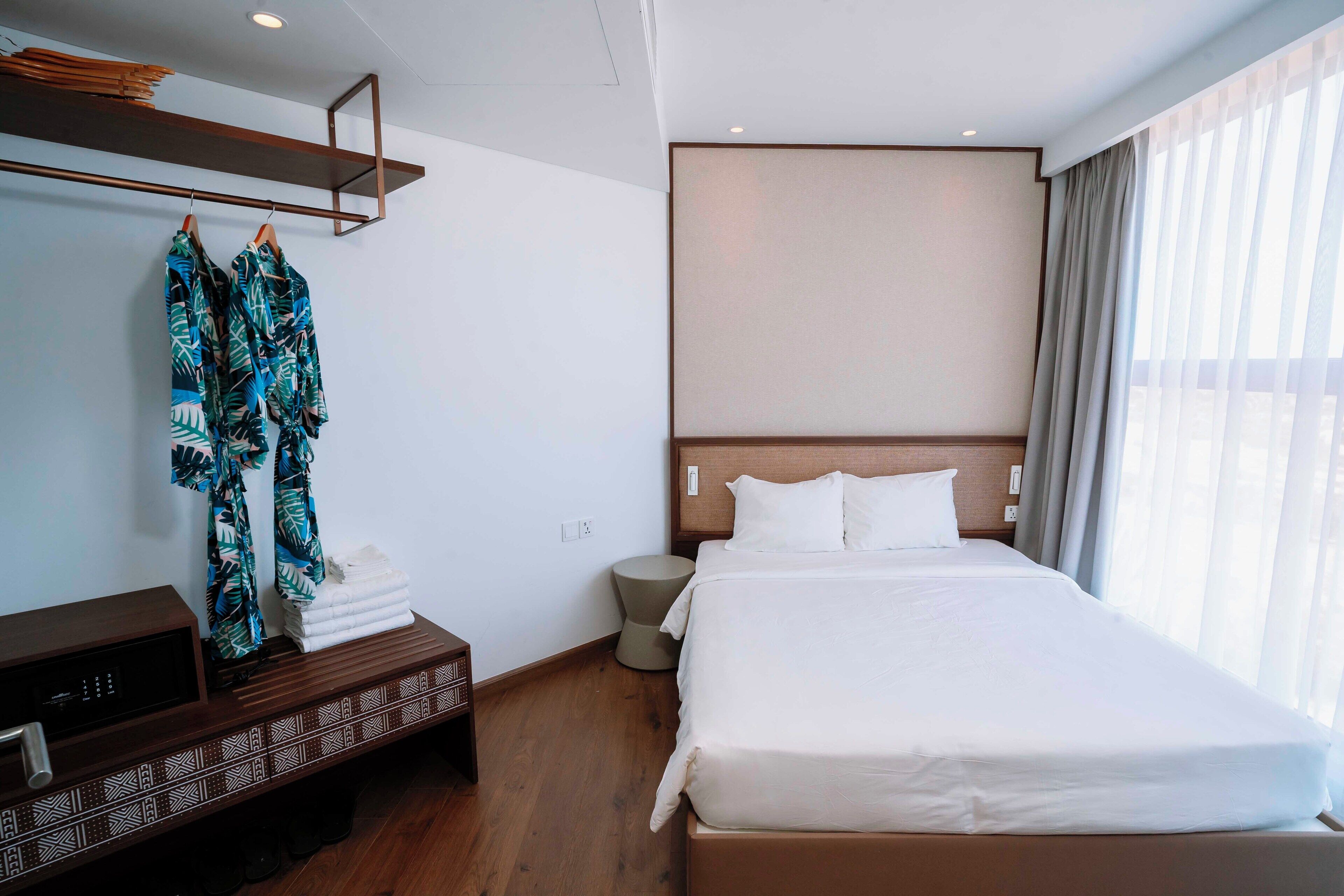 A hotel room with a bed, a bedside table, a wardrobe, and a large window with curtains.