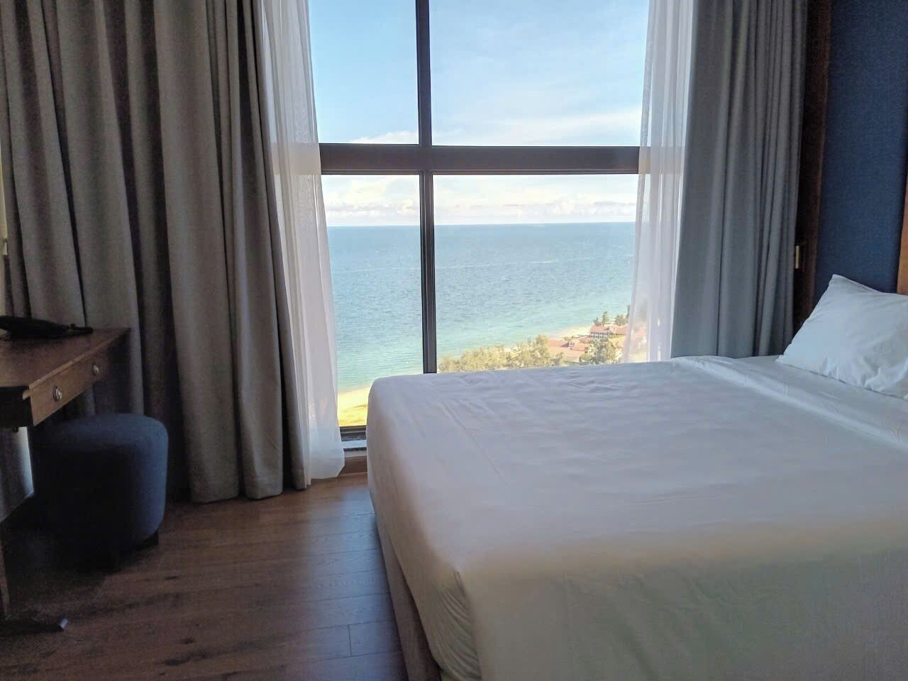 A bedroom with a large window, a bed, a desk, and a chair.