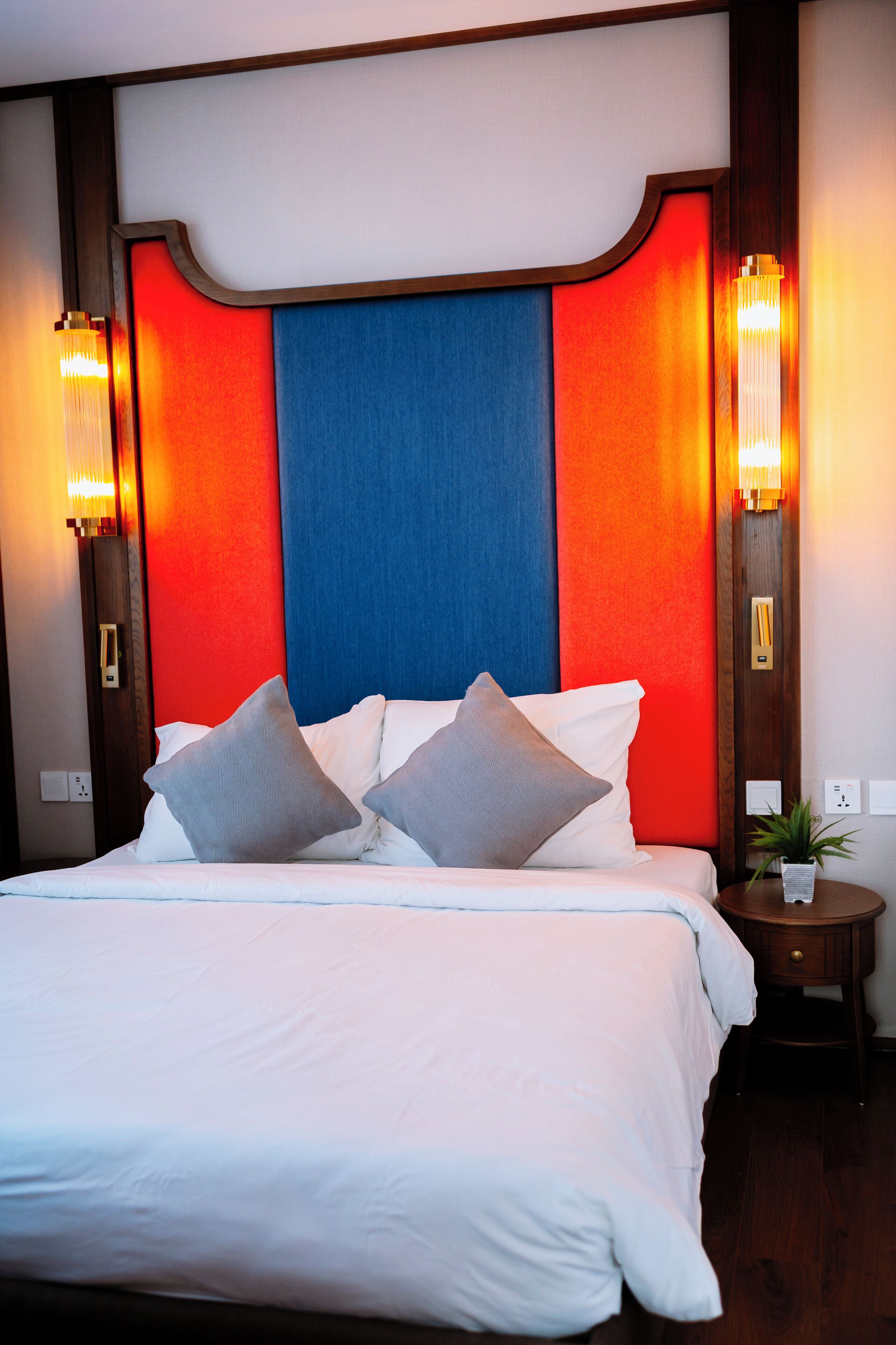 A hotel room with a large bed, two bedside lamps, and a nightstand with a plant.