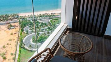 A balcony with a wicker chair and a small table, overlooking a beach and winding roads.