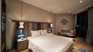 Habitación de hotel con una cama grande, lámparas de noche, un pequeño sofá, una mesita de noche y un adorno en la pared.