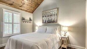Un dormitorio con una cama grande, una mesita de noche con lámpara, un radiador y una ventana con persianas.