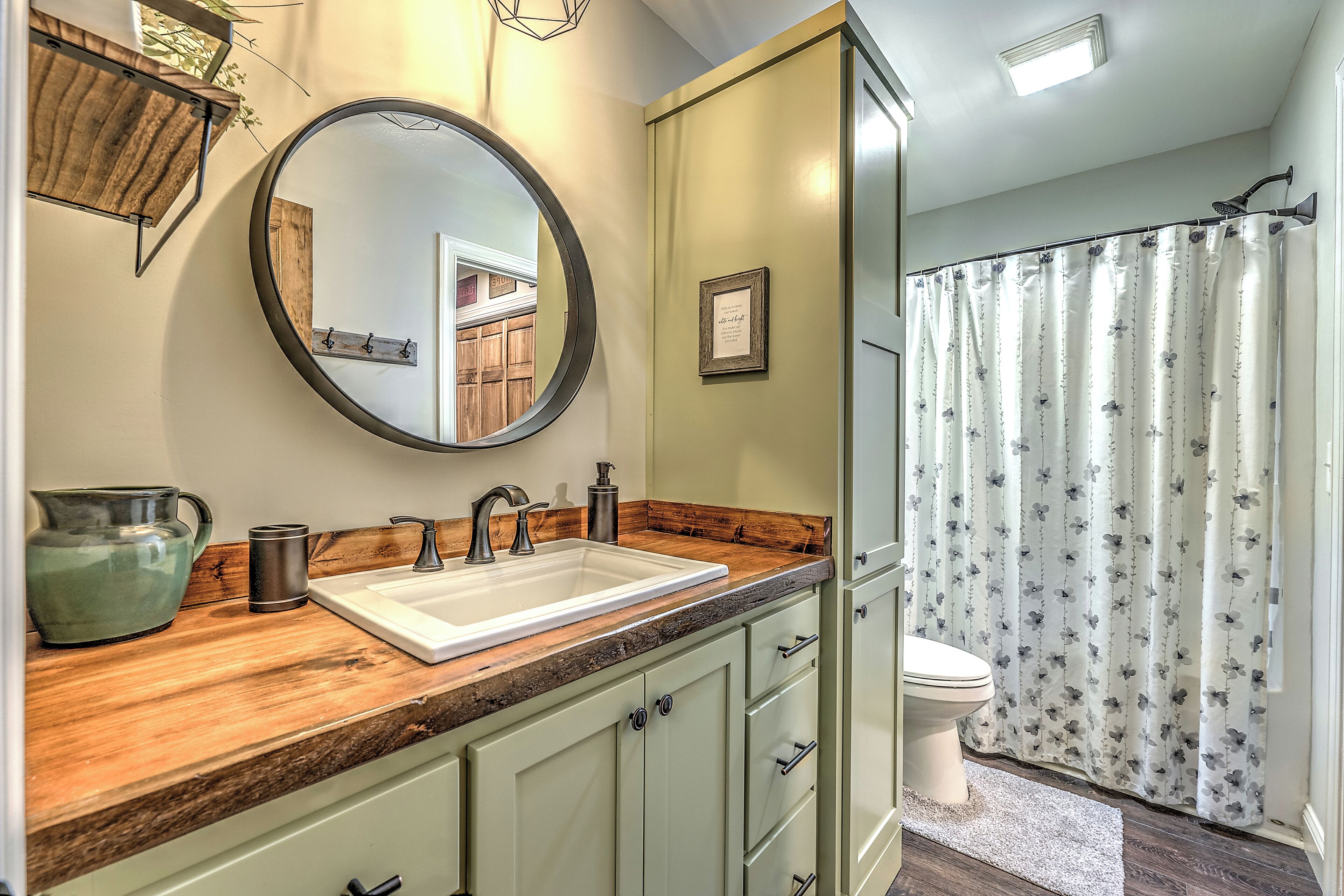 A bathroom with a wooden vanity, a round mirror, a sink, and a toilet.