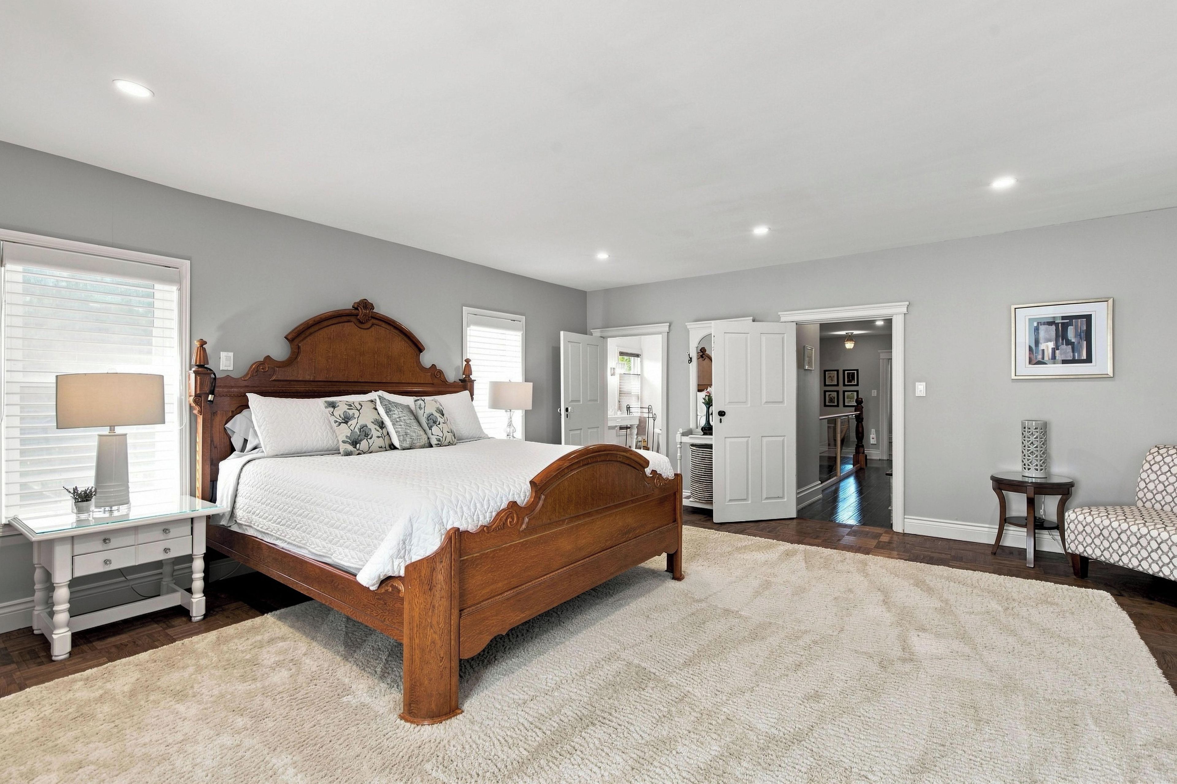 A bedroom with a large bed, bedside tables, a chair, and a door leading to another room.
