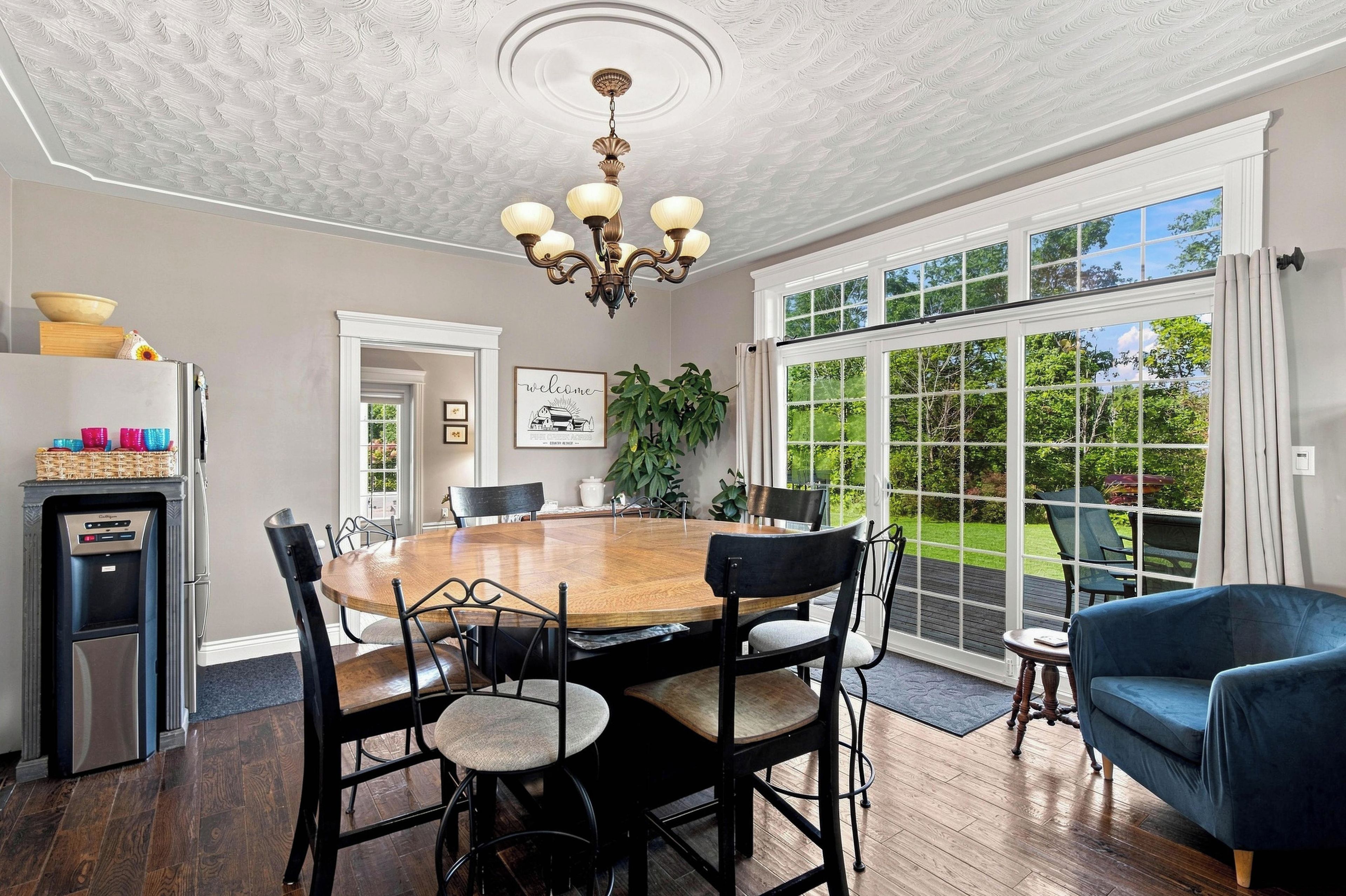 A dining area with a large wooden table, black chairs, a chandelier, and a view through large windows.