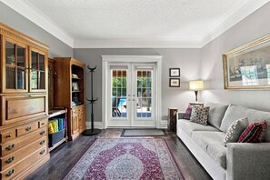 Een woonkamer met een grijze bank, een houten kast en een kamerkleed met een patroon.