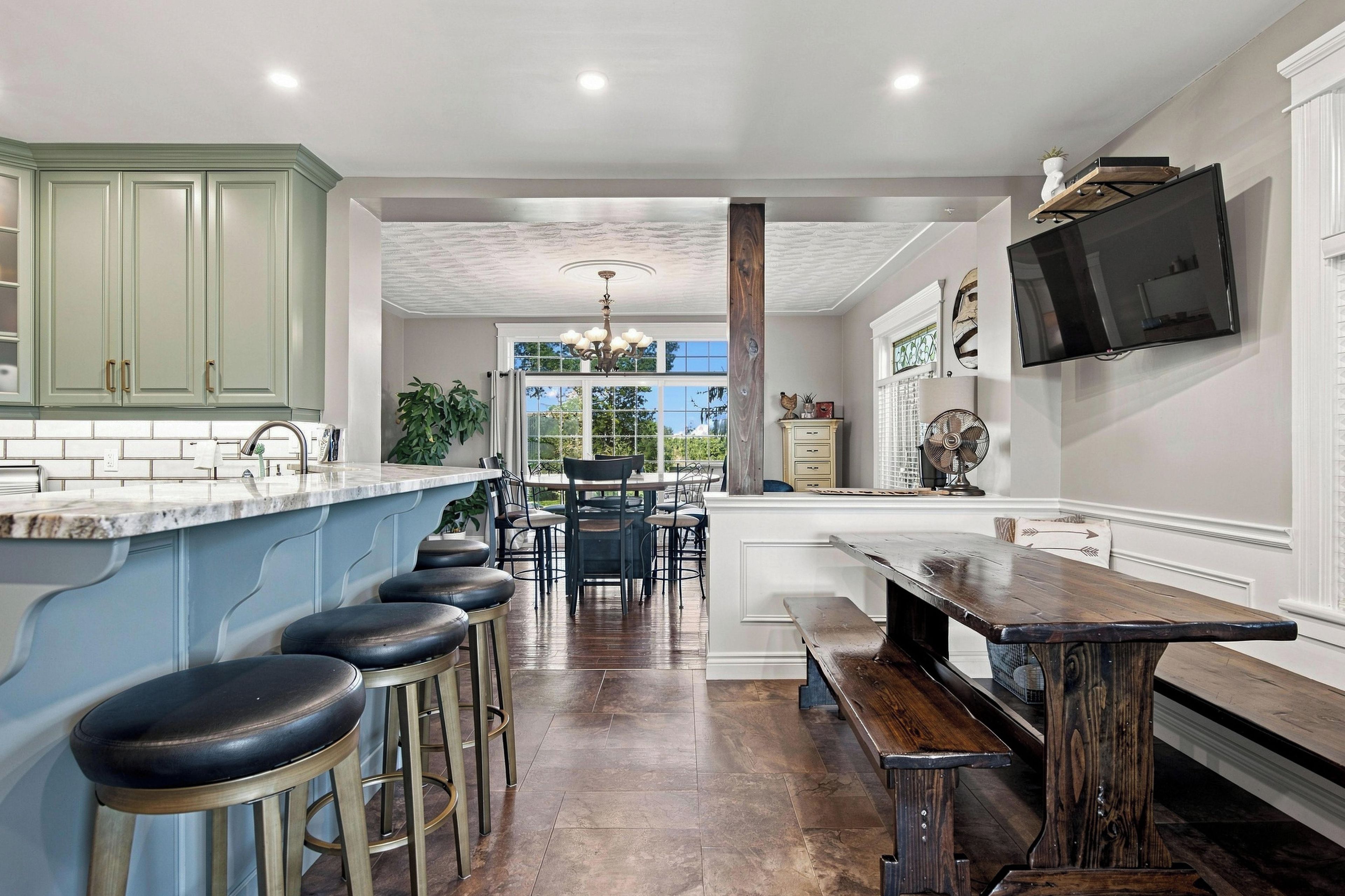 A modern kitchen with a bar area, wooden stools, and a large window.