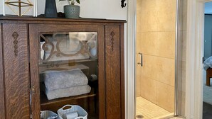 Ein Badezimmer mit Duschkabine aus Glas, einem Holzschrank mit Dekorationen und einem Handtuchhalter.