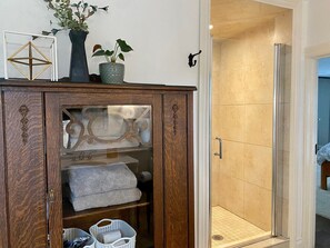 A bathroom with a glass shower enclosure, a wooden cabinet with decorative items, and a towel rack.