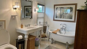 Ein Badezimmer mit Toilette, zwei Waschbecken, einer Badewanne, einem Spiegel und einem gerahmten Bild an der Wand.