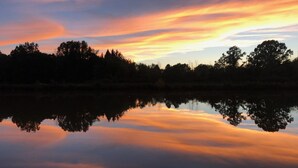 Ein ruhiger See spiegelt einen Sonnenuntergangshimmel wider, wobei Bäume am Horizont silhouettiert sind.