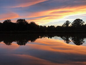 A calm lake reflecting a sunset sky with trees silhouetted against the horizon.