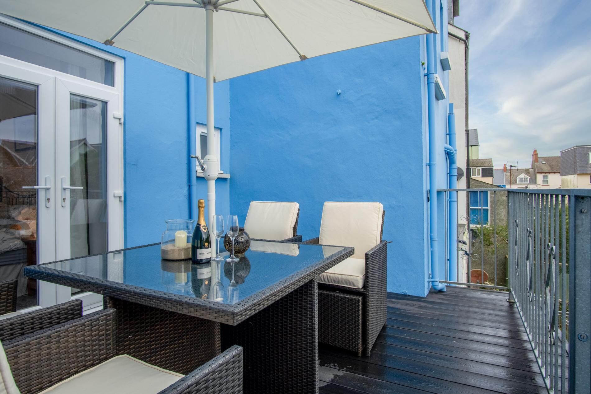 A balcony with a glass table, two wicker chairs, and a white umbrella.
