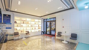 A lobby with a marble floor, white walls, and shelves with books and decorative items. There are several chairs and tables arranged for seating. - XiYuan Hotel (Beijing)